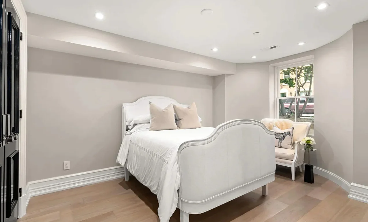 The bedroom as it is, with a white upholstered bed and bare walls, before its redesign